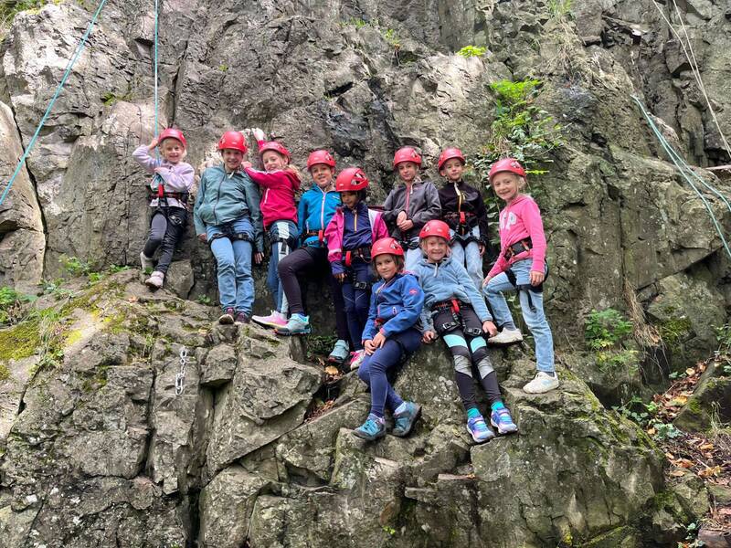 Eine Gruppe von Kindern mit roten Helmen und Kletterausrüstung posiert auf einer felsigen Oberfläche.