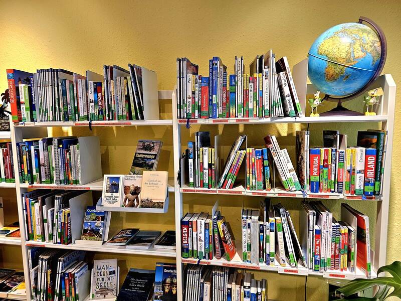 Ein Bücherregal voller Reiseführer und Bildbände ist zu sehen, mit einem Globus auf dem oberen Regal.