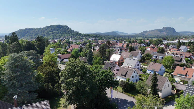 Eine luftige Aussicht auf ein grünes Wohngebiet mit zahlreichen Häusern und bewaldeten Hügeln im Hintergrund.