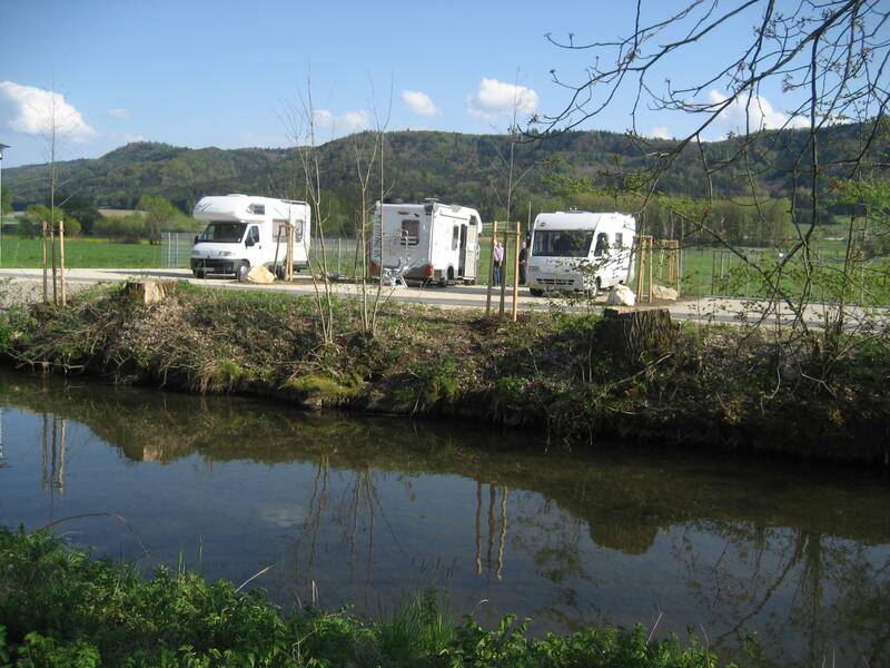 Drei Wohnmobile stehen auf dem Wohnmobilstellplatz bei Naturbad Aachtal neben der Aach vor dem Schienerberg.